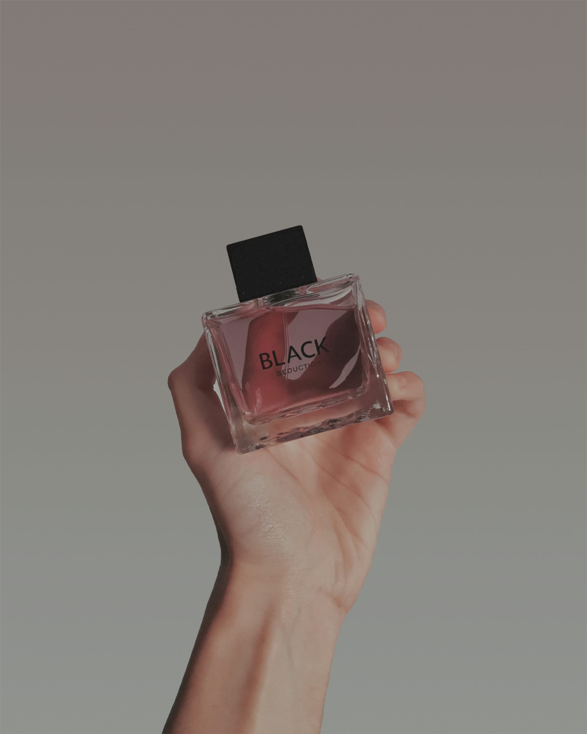 a hand holding a bottle of black perfume